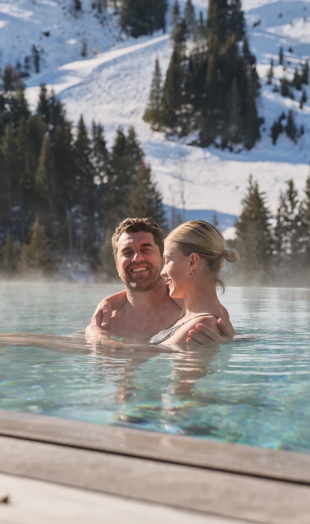 Paar im Außenpool vor verschneiter Berglandschaft