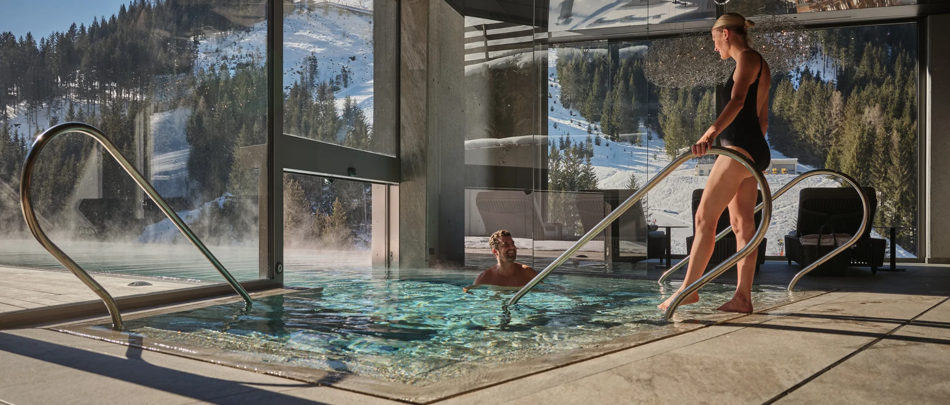 Frau steigt aus Pool im Sporthotel Wagrain mit Blick auf verschneite Berge