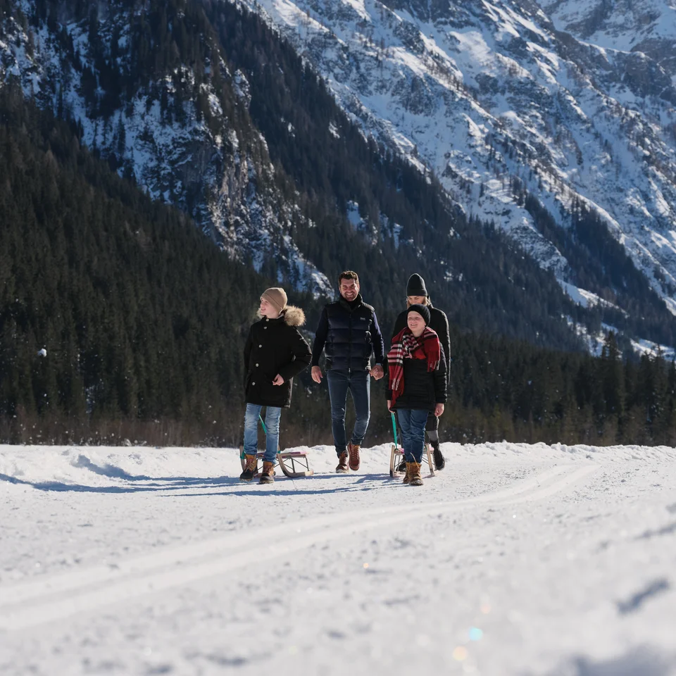 Family with sled in the snow in front of mountain backdrop