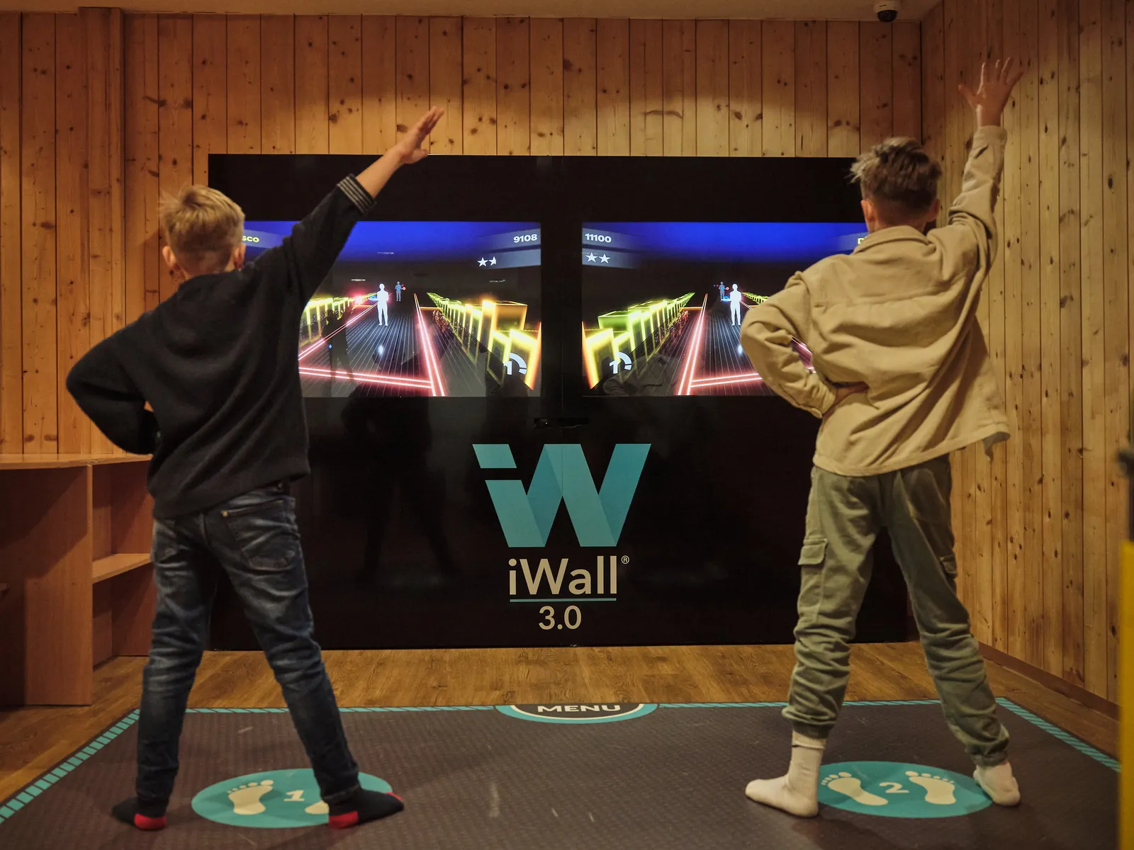 Zwei Jungen spielen mit erhobenen Armen an einer iWall 3 im Sporthotel Wagrain