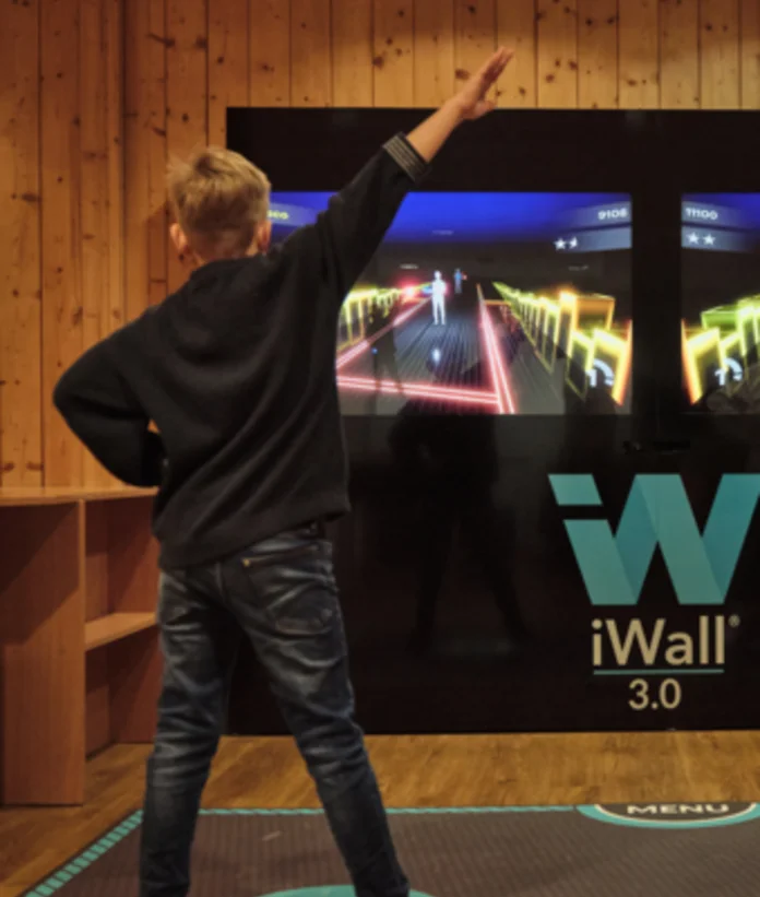 Zwei Jungen spielen mit erhobenen Armen an einer iWall 3 im Sporthotel Wagrain