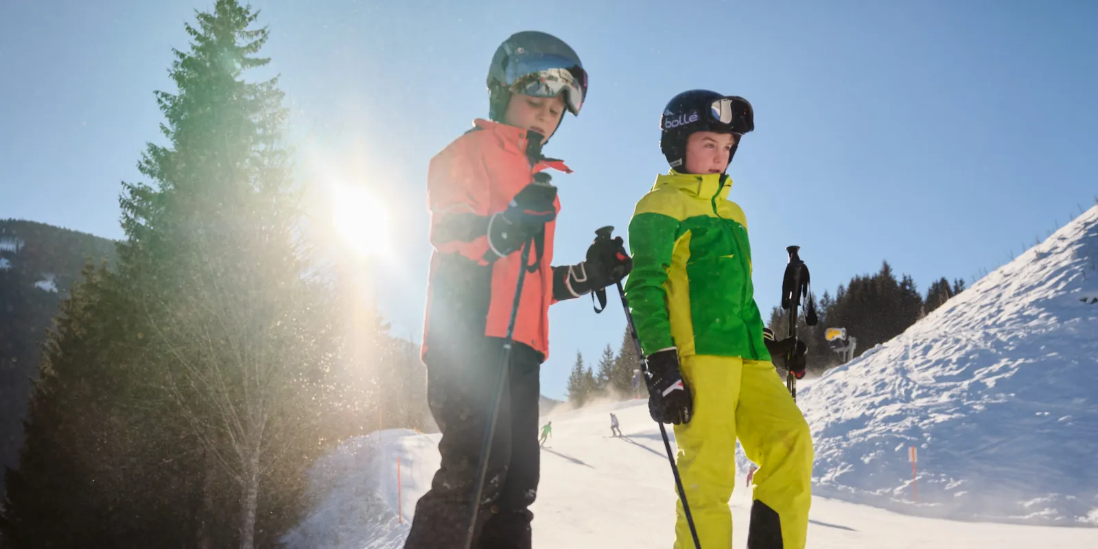 Two children with skis on a snow-covered slope in the sunshine