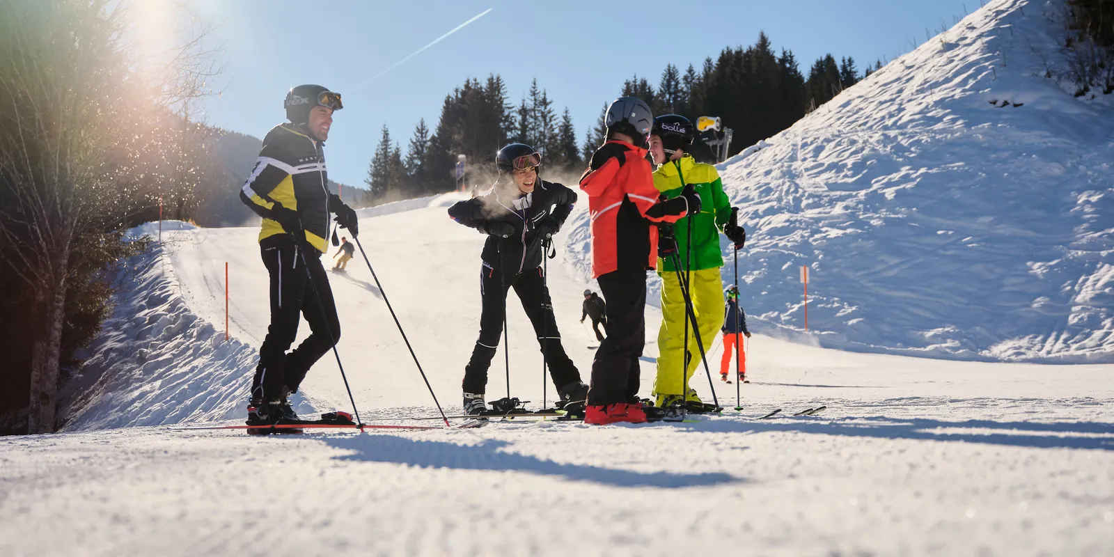 Skiers standing on a ski slope in front of a wooded hill