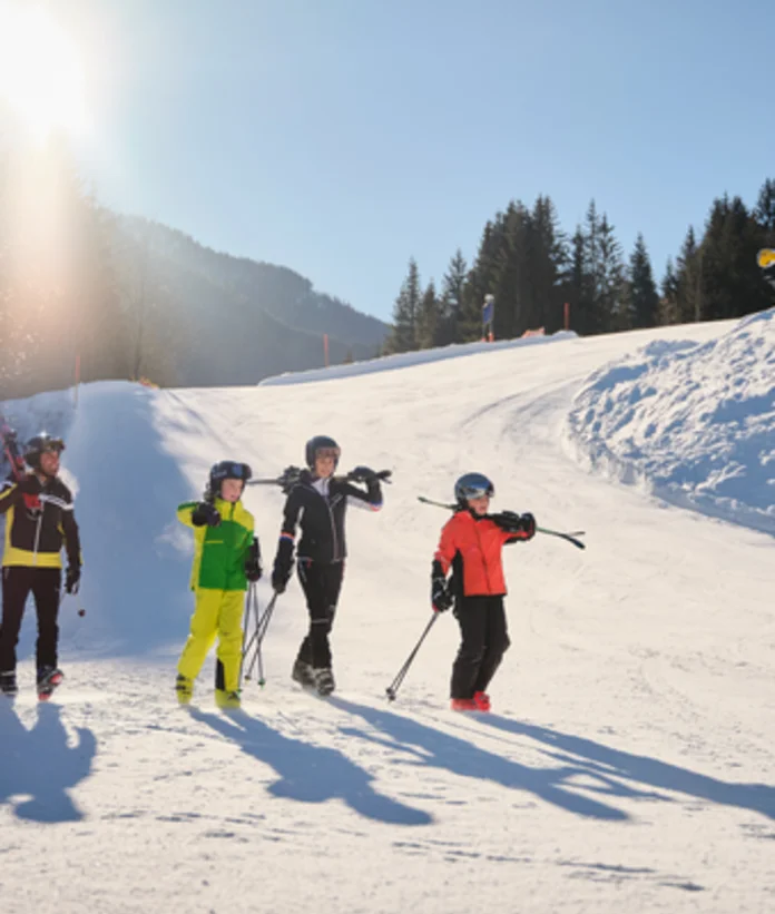 Familie mit Skiern und Stöcken auf schneebedeckter Piste vor Bergkulisse