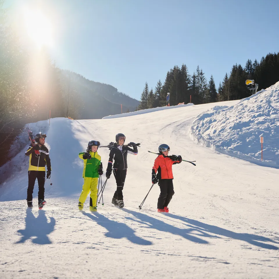 Family with skis and poles on a snow-covered slope in front of a mountain backdrop