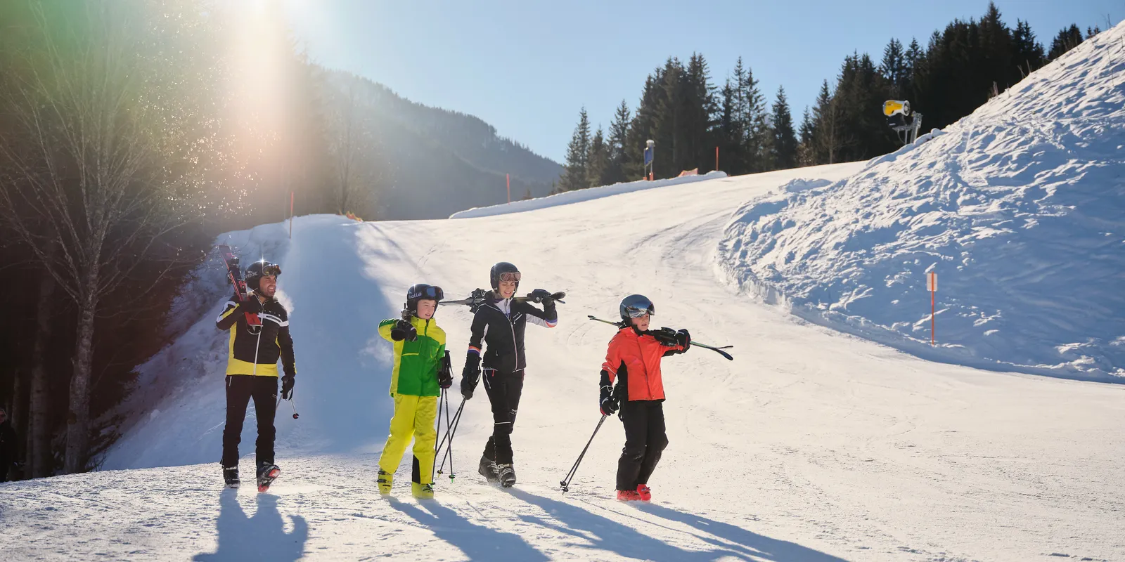 Familie mit Skiern und Stöcken auf schneebedeckter Piste vor Bergkulisse