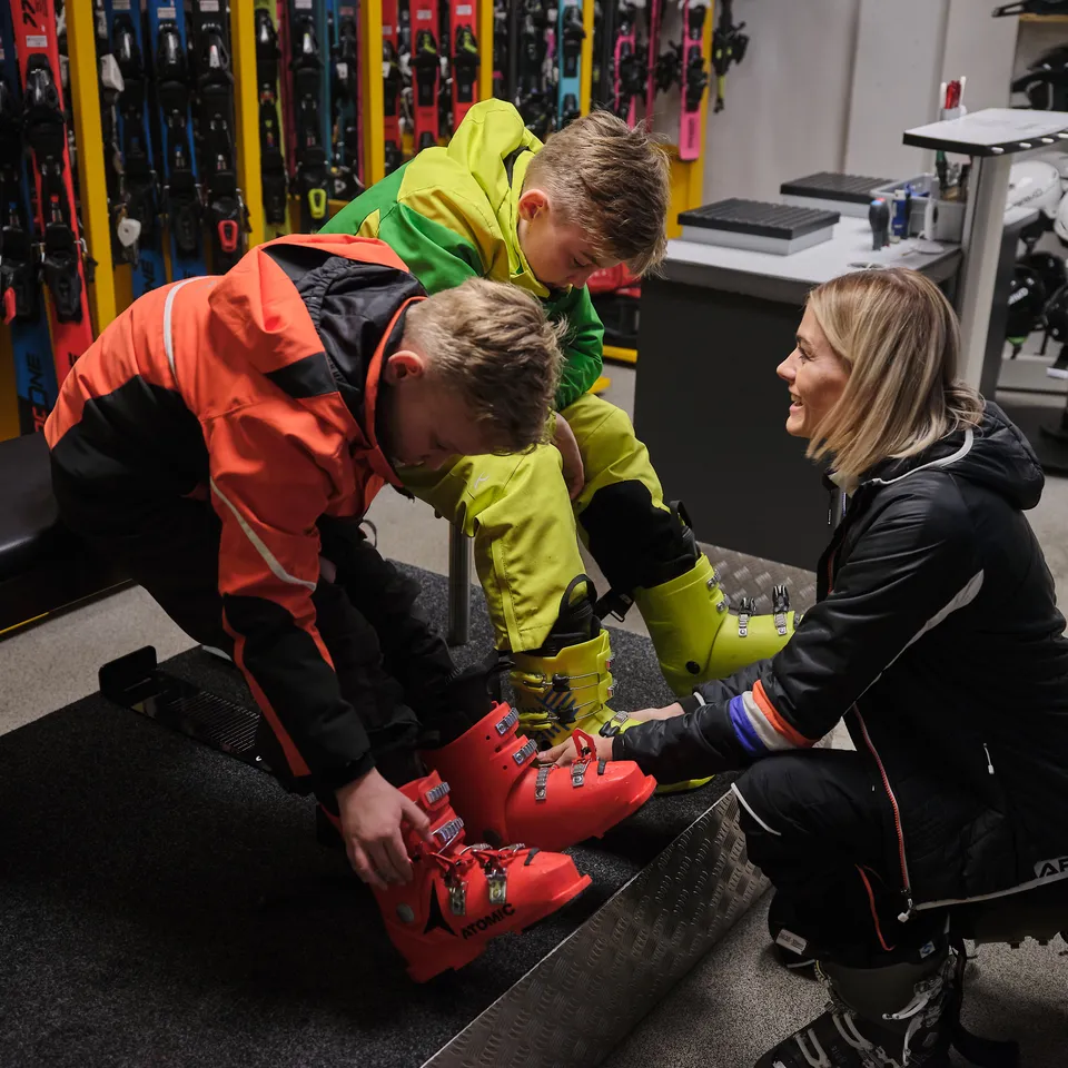 Frau hilft zwei Jungen beim Anziehen von Skischuhen in einem Skiverleih